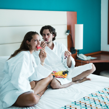 Two people sitting on a double bed in a hotel room