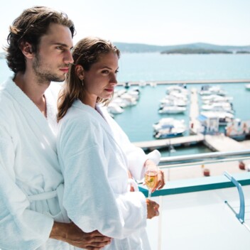 A man and a woman standing on a balcony in bathrobes with a view of the marina