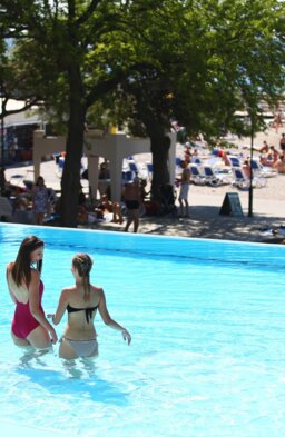 Two women walking through the shallow part of an outdoor pool by the beach